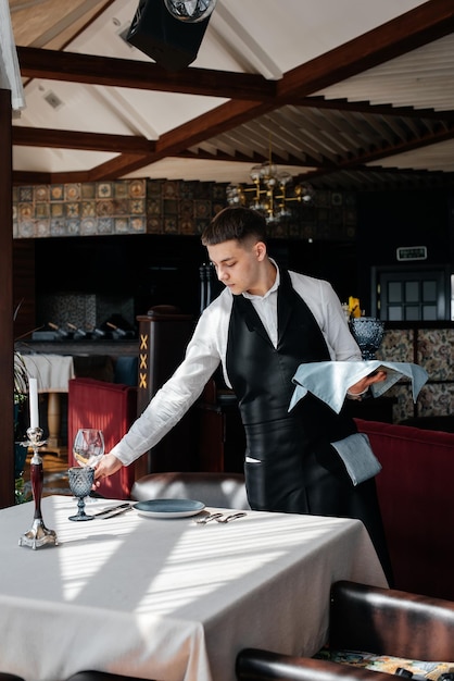 A young male waiter in a stylish uniform is engaged in serving\
the table in a beautiful gourmet restaurant a highlevel restaurant\
table service in the restaurant