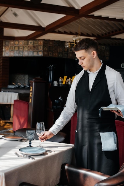 A young male waiter in a stylish uniform is engaged in serving the table in a beautiful gourmet restaurant A highlevel restaurant Table service in the restaurant