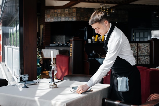 A young male waiter in a stylish uniform is engaged in serving the table in a beautiful gourmet restaurant A highlevel restaurant Table service in the restaurant