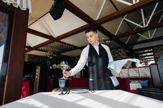 A young male waiter in a stylish uniform is engaged in serving the table in a beautiful gourmet restaurant. Restaurant activity, of the highest level.