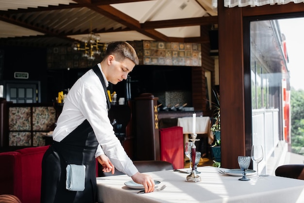 Un giovane cameriere in un'elegante uniforme è impegnato a servire la tavola in un bellissimo ristorante gourmet. attività di ristorazione, di altissimo livello.