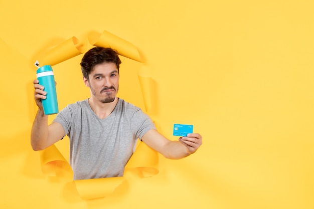 young male with credit card and impressed with waters taste on a yellow background sale athlete