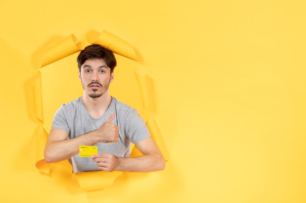 Photo young male with credit card on a torn yellow paper background money bank sale shopping