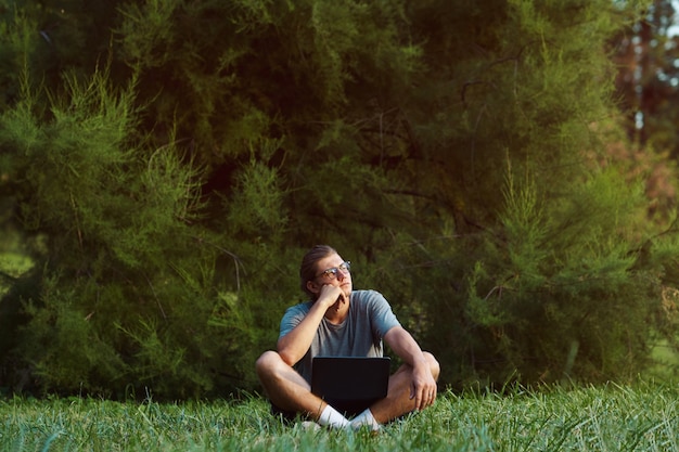 Young male with notebook sitting on grass in public park