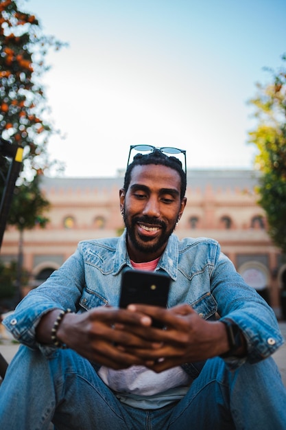 Young male with sunglasses sitting on the street using smartphone to see social media