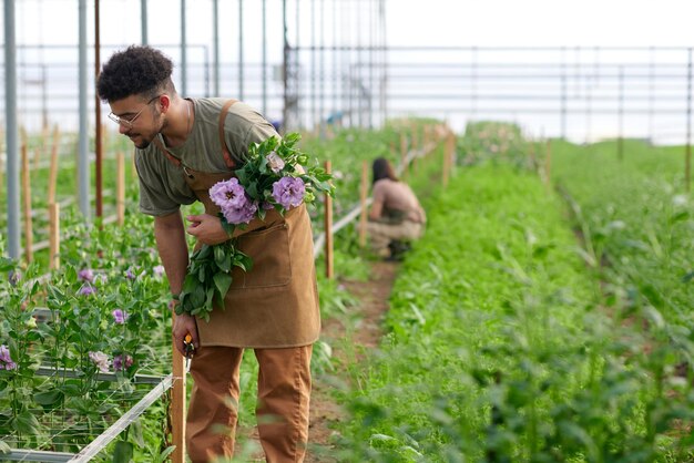 Young male worker of garden center bending over flowerbed