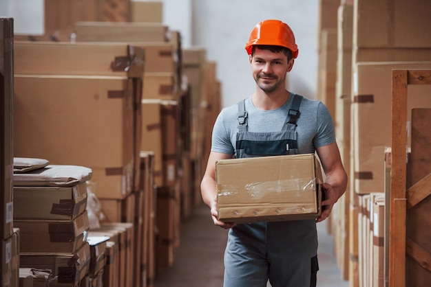 Young male worker in uniform is in the warehouse with box in hands.