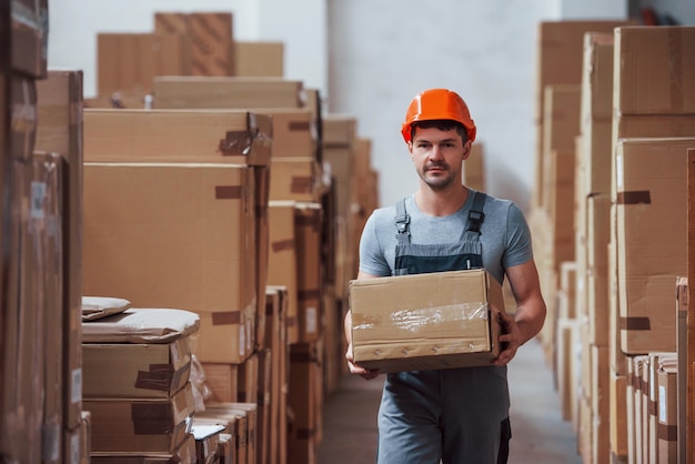 young male worker in uniform is in the warehouse with box in hands.