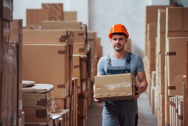 Young male worker in uniform is in the warehouse with box in hands.