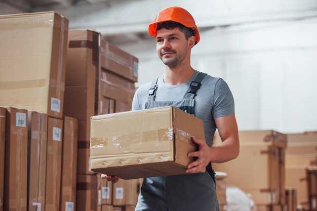 Young male worker in uniform is in the warehouse with box in hands.