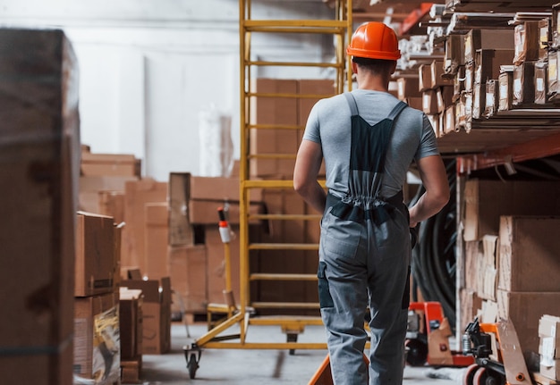 Young male worker in uniform is in the warehouse with pallet truck.