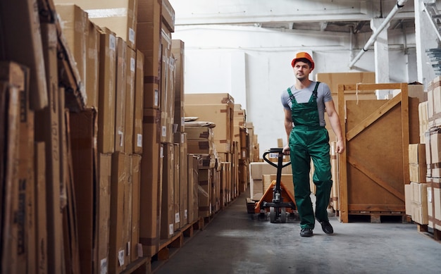 Young male worker in uniform is in the warehouse with pallet truck.