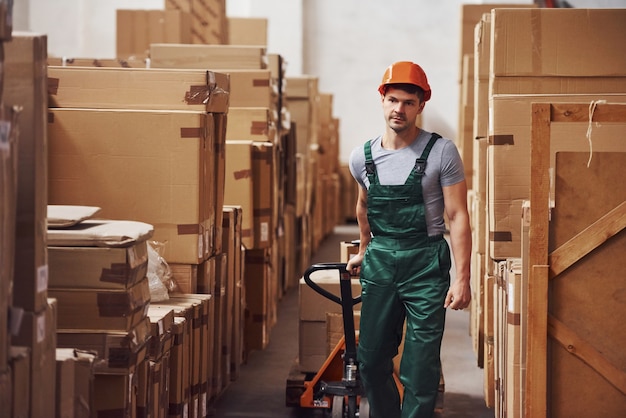 Young male worker in uniform is in the warehouse with pallet truck.