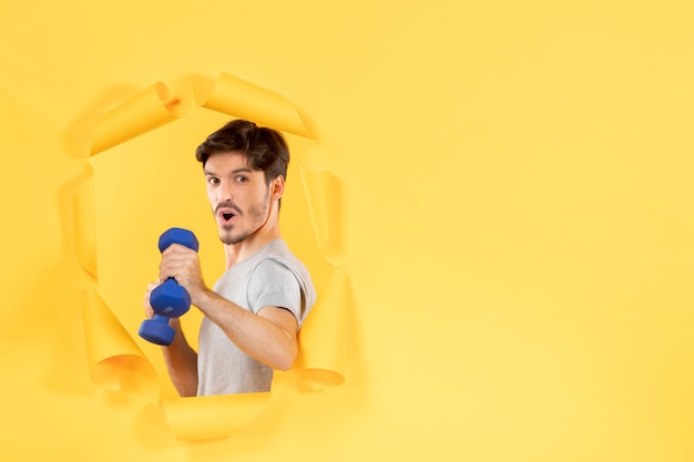 young male working out with blue dumbbells on yellow background sport athlete gym exercise fit