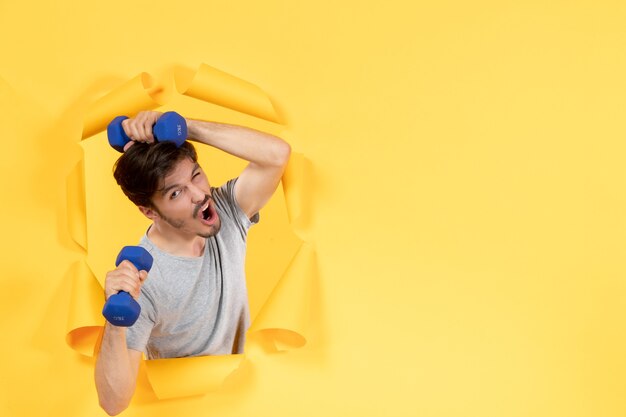 Young male working out with blue dumbbells on yellow desk athlete exercise sport gym