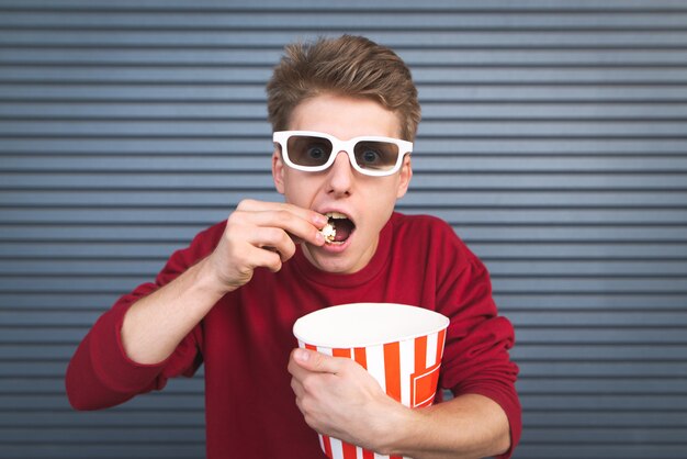 young man in 3D glasses eating popcorn from a bowl