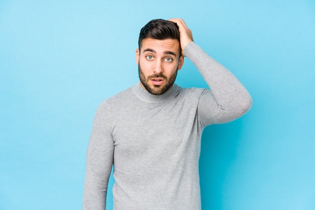 Young man against a blue wall isolated tired and very sleepy keeping hand on head