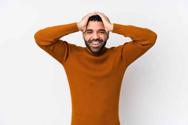 Young man against a white laughs joyfully keeping hands on head. Happiness concept.