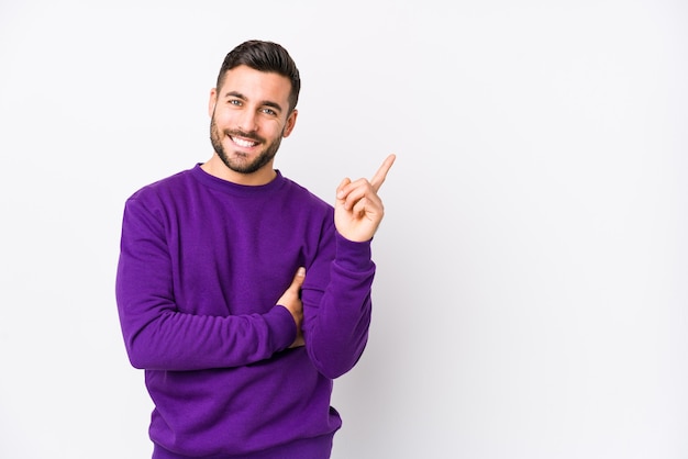 Giovane uomo contro un muro bianco isolato sorridendo allegramente indicando con l'indice lontano