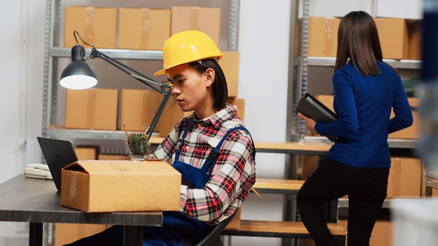 Young man analyzing products in boxes before shipment, checking warehouse stock for distribution on laptop. Depot employee doing quality control, helping with supply chain. Handheld shot.