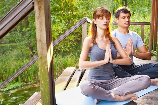 写真 ヨガをしている若い男性と女性。蓮華座は庭で瞑想をします。屋外全身