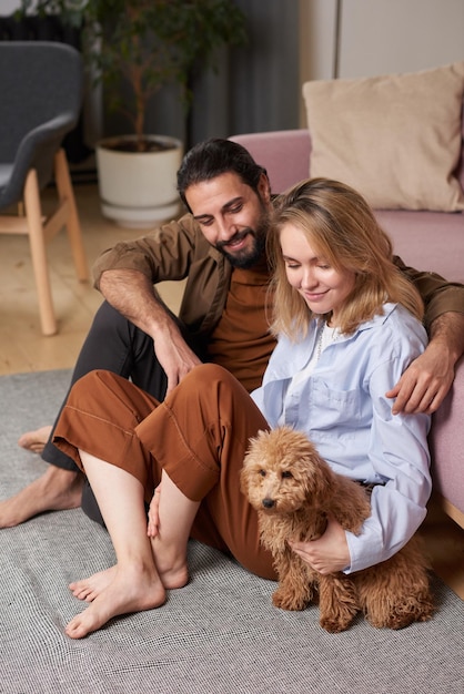 Фото Молодой мужчина и женщина проводят свободное время вместе дома, сидя на полу в гостиной, расслабляясь со своей собакой