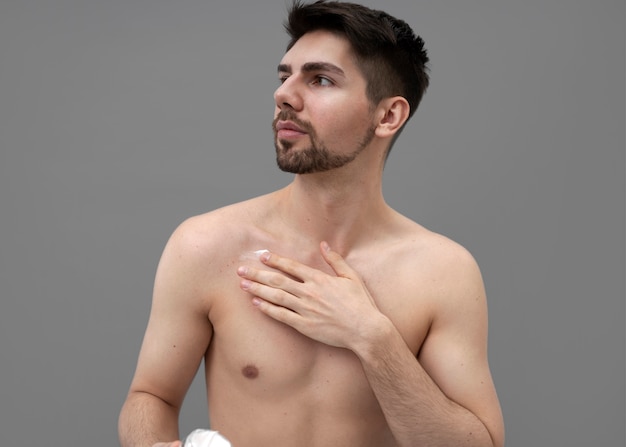 Photo young man applying shiny lotion on his chest