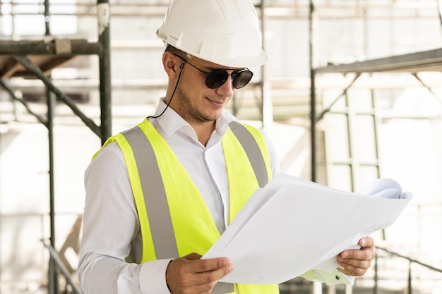 Young man architect wearing safety vest with a blueprints on a construction site