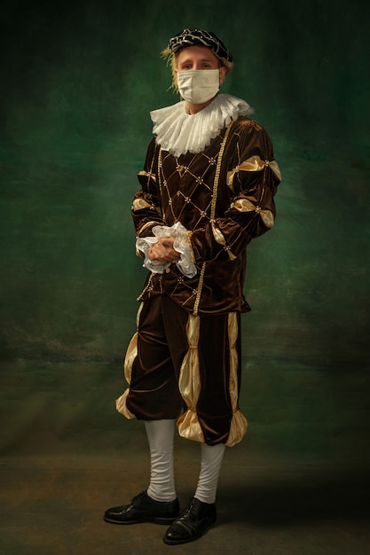 Photo young man as a medieval knight on dark background wearing protective mask against coronavirus