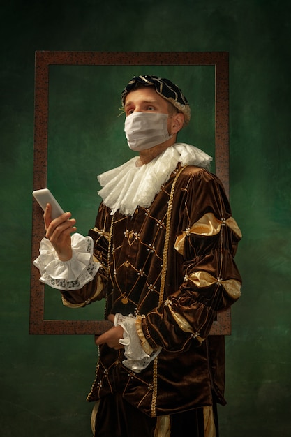 Young man as a medieval knight on dark background wearing protective mask against coronavirus