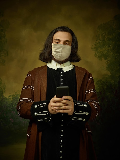 Молодой человек как средневековый рыцарь на темном фоне в защитной маске от коронавируса