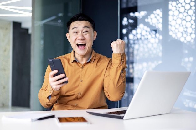 A young man an asian office worker plays online games on the phone rejoices at the victory he points