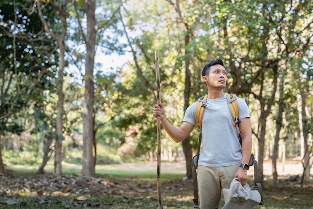 Молодой человек азиатский трекинг среди деревьев с рюкзаком молодой человек наслаждается в одиночестве в лесу кемпинг пешие прогулки путешествие в поисках приключений концепция.