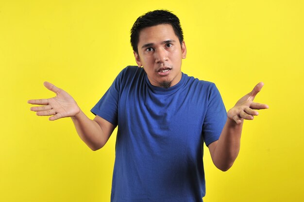 Young man asking questions with hands raised, isolated on yellow background