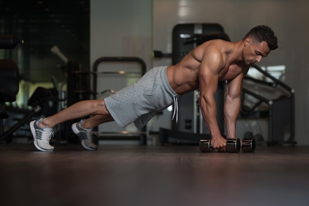 Young Man Athlete Doing Pushups With Dumbbells As Part Of Bodybuilding Training