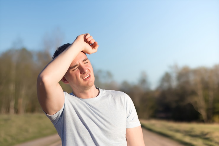 Young man athlete received sun and heat stroke and headache. guy holds his head with his hands and protects himself from the sun in outdoors.