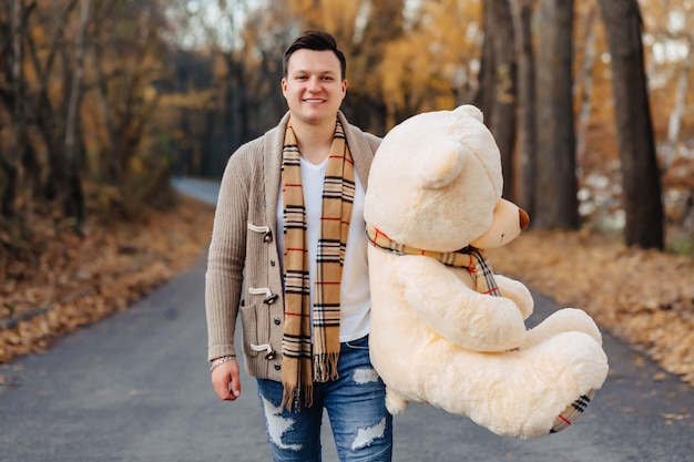 Young man at autumn park road with big bear toy