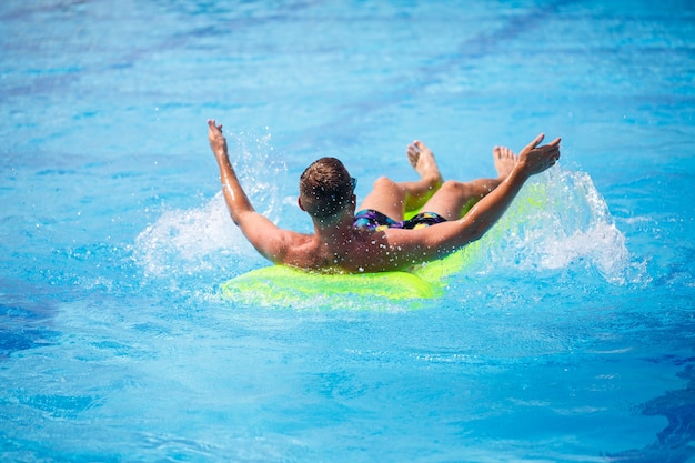 A young man bathes in the pool on a yellow inflatable mattress. Relax in the bright sun on vacation. Happy successful guy. Selective focus