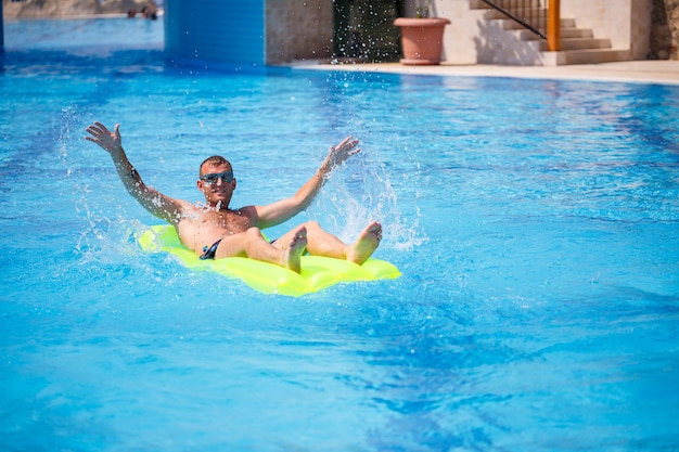 A young man bathes in the pool on a yellow inflatable mattress