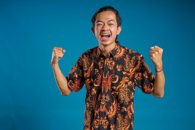 Young man in batik shirt celebrates victory while raising both hands