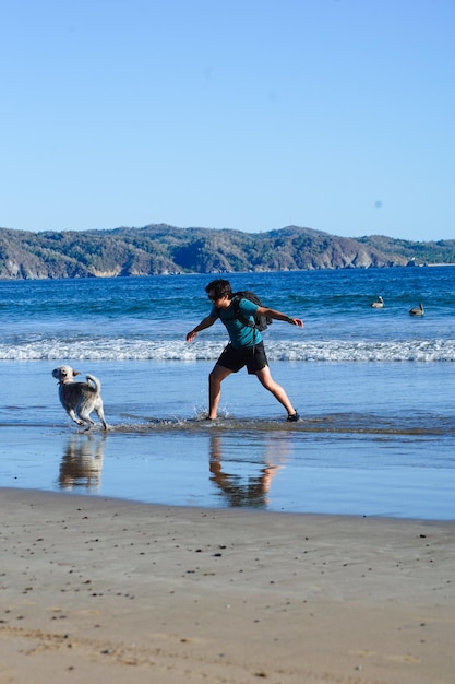 Foto giovane sulla spiaggia con il suo cane e la borsa fotografica