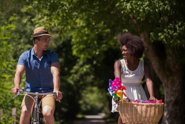 молодой человек и красивая афроамериканская девушка наслаждаются велосипедной прогулкой на природе в солнечный летний день