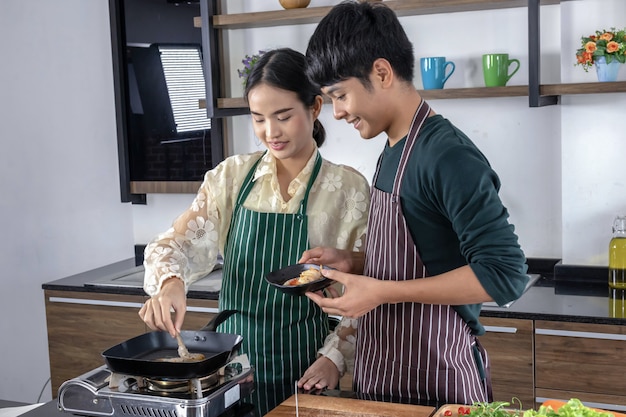 A young man and a beautiful asian teenager is happy to make shrimp salad in a modern kitchen.