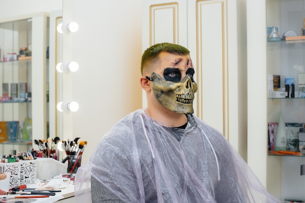 スタジオのクローズアップでハロウィーンの休日のための頭蓋骨の形で美しい不気味な化粧をしている若い男。ハッピーハロウィンのコンセプト。