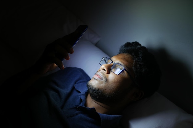 夜にスマートフォンを使用してベッドの上の若い男