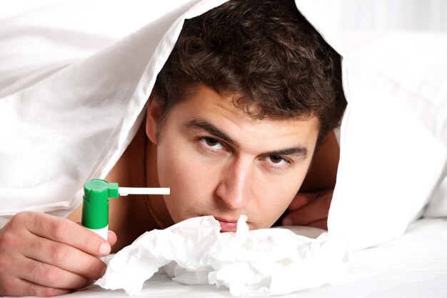 A young man in bed with sore throat over white background