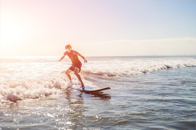 Young man, beginner Surfer learns to surf on a sea foam on the Bali island