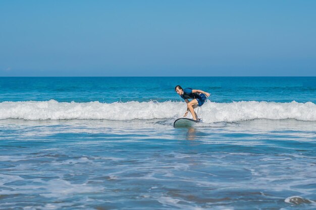 젊은 남자, 초보자 서퍼는 발리 섬의 바다 거품에서 서핑을 배웁니다.