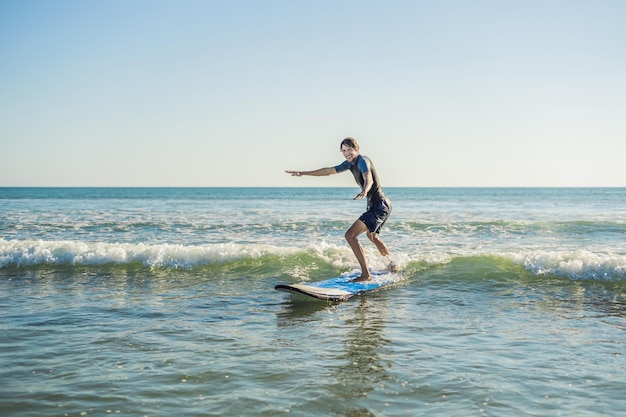 Young man, beginner Surfer learns to surf on a sea foam on the Bali island