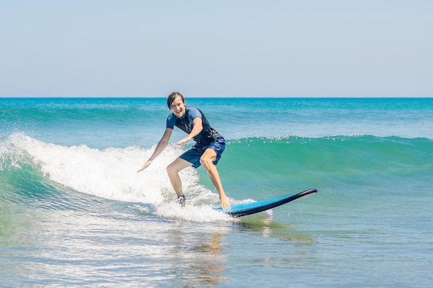 Young man, beginner Surfer learns to surf on a sea foam on the Bali island